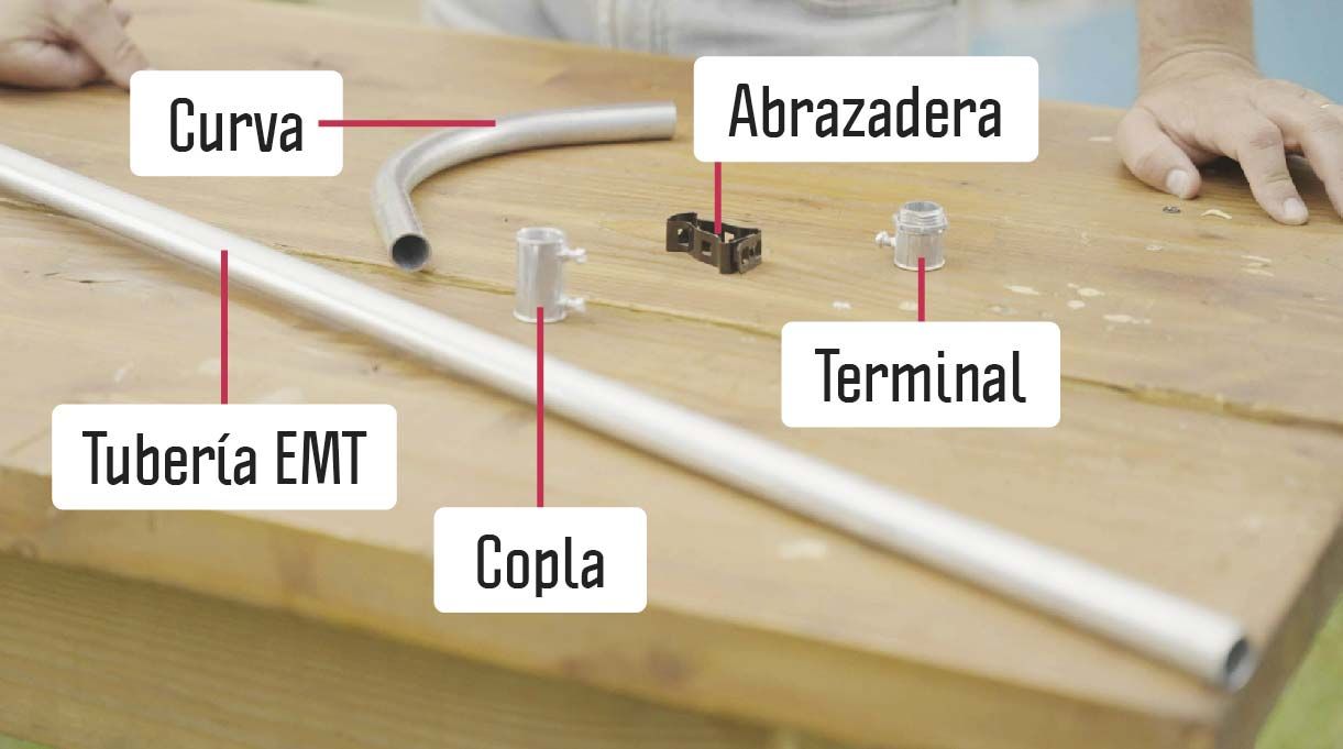 curva, abrazadera, terminal, tubería EMT y copla sobre una mesa de madera