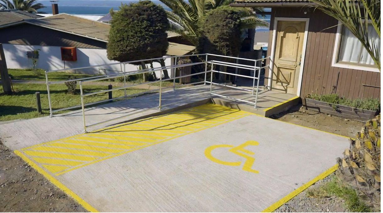 rampa con acceso universal terminada, con simbolo de persona en silla de ruedas pintado en amarillo y franja amarilla en un costado.