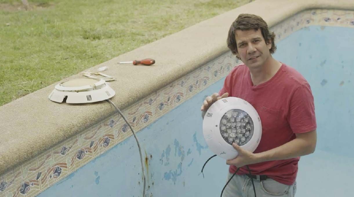 Droste dentro de la piscina vacía sosteniendo en sus manos el foco a instalar