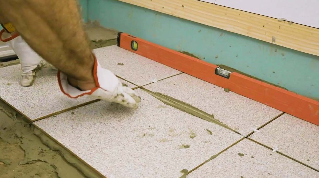 Se muestran las manos de una persona instalando cerámica en el piso