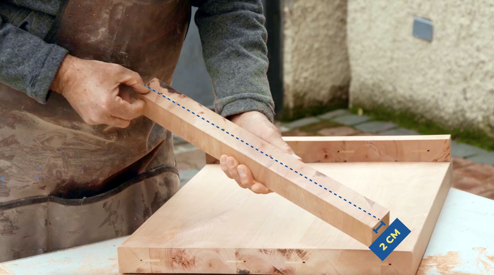 Una persona mostrando el sobrante de la tabla de madera y los 2 cm que cortará para hacer faldón
