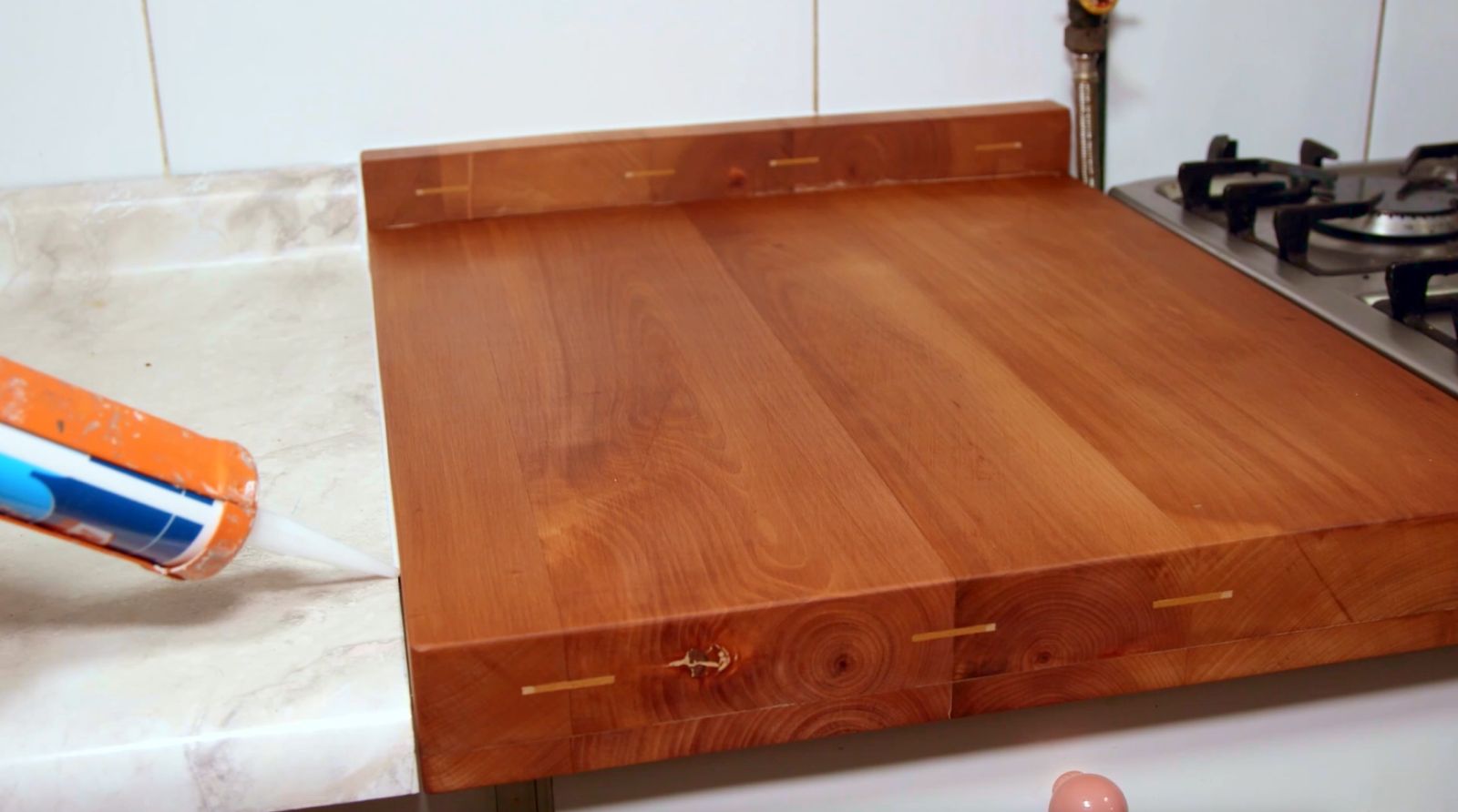 Se ve la tabla de madera terminada en el mesón de melamina. Una persona aplica silicona en el borde.