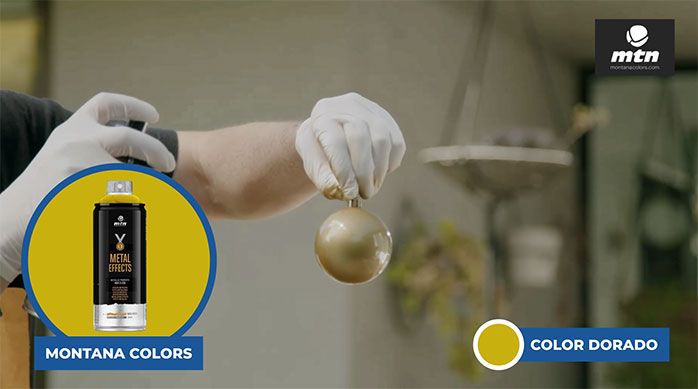 Una persona aplicando spray color dorado de Montana Colors en la decoración navideña