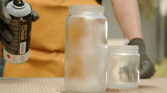 Una persona aplica spray con efecto esmerilado en frascos de vidrio
