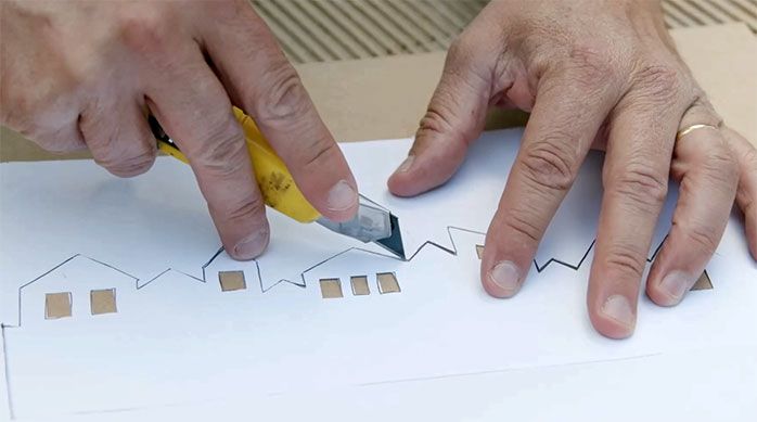 Una persona corta con cuchillo cartonero el perfil de un dibujo de casas