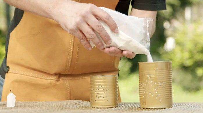Una persona pone arena dentro de las latas de conserva doradas