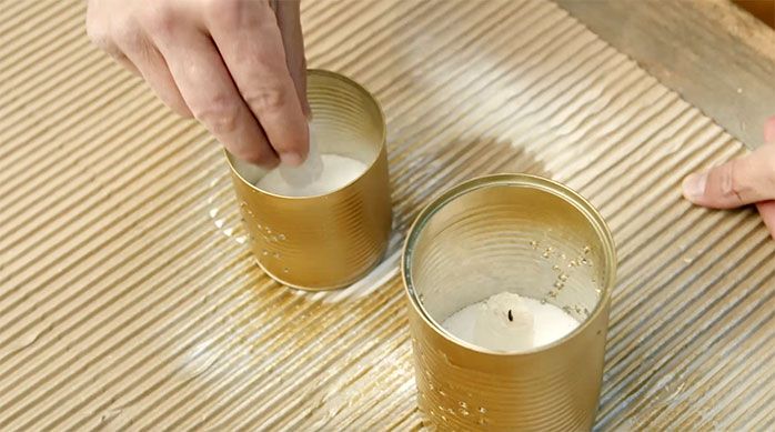 Una persona pone velas dentro de las latas doradas