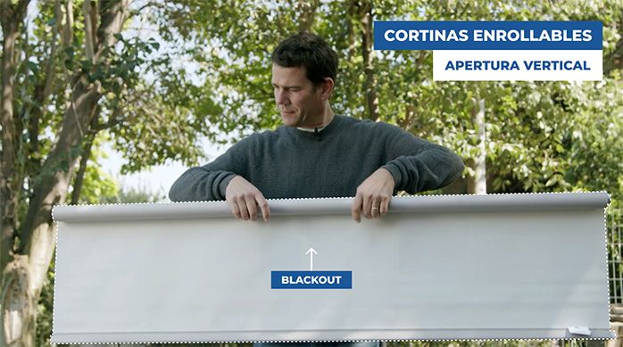 Una persona muestra una cortina enrollable o roller de tela blackout