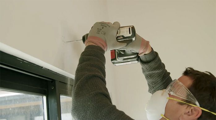 Una persona perfora el muro para instalar la cortina enrollable o roller
