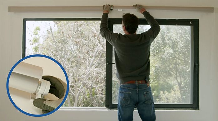 Una persona monta la cortina roller en los soportes sobre la ventana