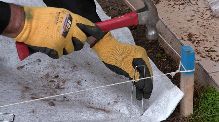 Una persona martilla una estaca para fijar la barrera anti maleza en el jardín de piedras