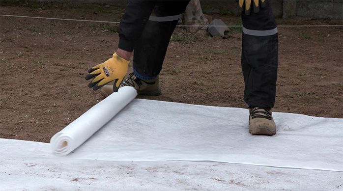 Una persona desenrolla la malla de geo textil anti maleza en el jardín de piedras
