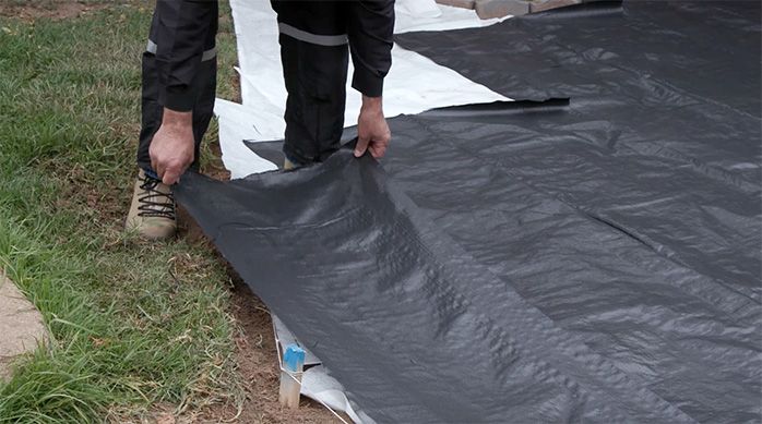 Una persona pone la tela negra ground cover anti maleza sobre la malla blanca geo textil