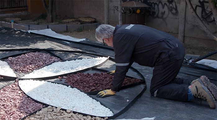 Una persona distribuye gravilla roja en los pétalos de la flor del jardín de piedras