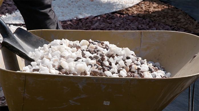 Una persona mezcla diferentes tipos de piedra en una carretilla con una pala