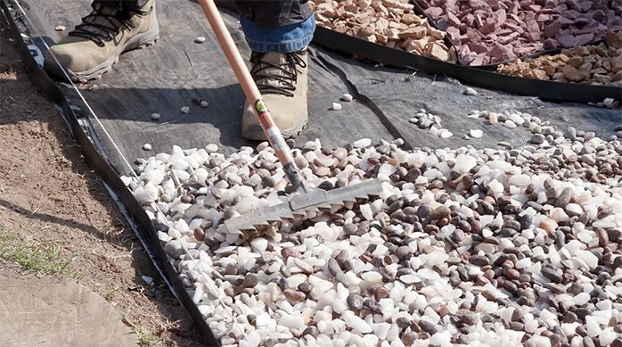 Una persona distribuye las piedras en el jardín de piedras con un rastrillo