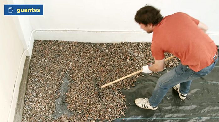 Una persona esparce las piedras con un rastrillo sobre la malla de polietileno