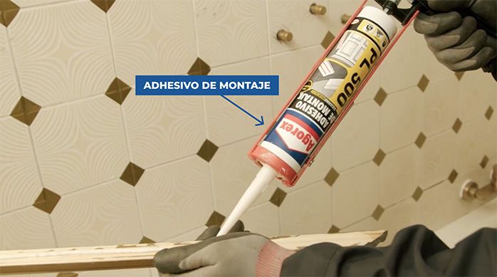 Una persona aplica adhesivo de montaje en una moldura de madera