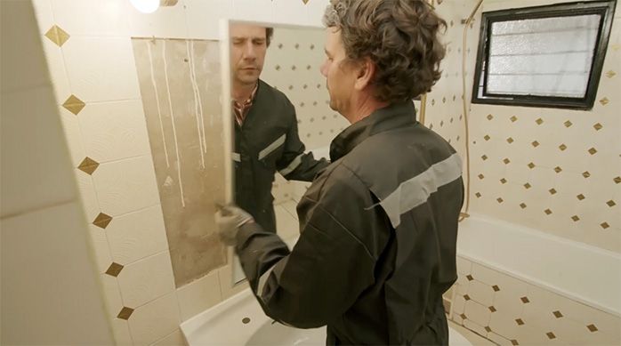 Una persona desmonta el espejo grande para renovarlo en el baño moderno