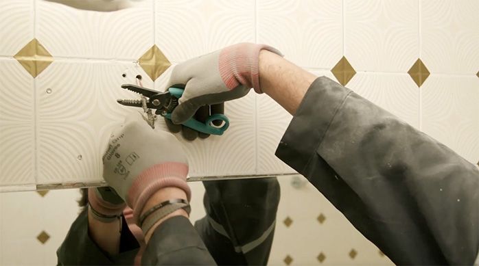 Una persona corta el cable eléctrico de la luz del espejo con un pelacable