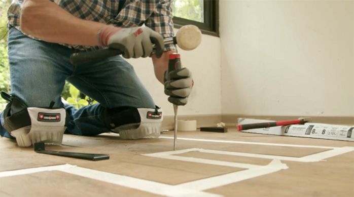 Una persona introduce un formón entre las tablas del piso laminado para empezar a retirarlo