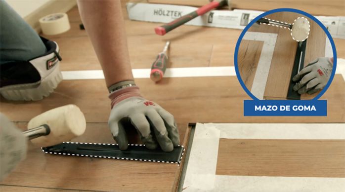 Una persona golpea la barra tensora para desencajar el piso laminado dañado por la humedad