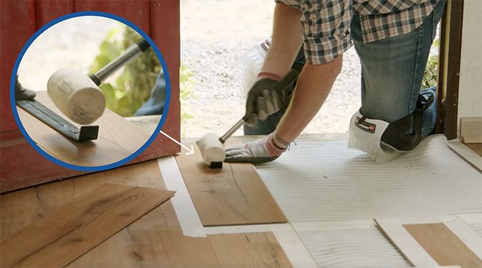 Una persona golpea la barra tensora para encajar la tabla de piso laminado
