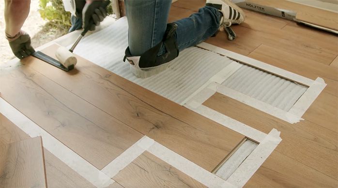 Una persona golpea la barra tensora con un mazo de goma para encajar las tablas de piso laminado
