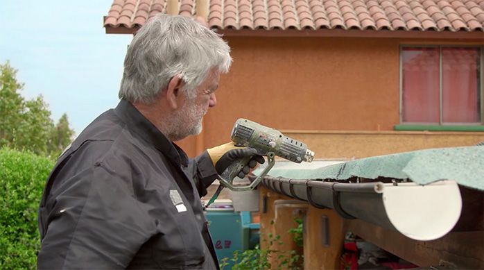 Una persona calienta el borde de la membrana asfáltica con una pistola de calor