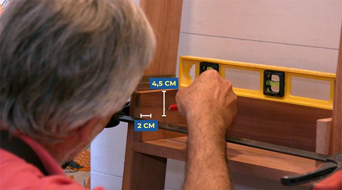 Una persona marca el lugar de las fijaciones en la primera repisa del organizador para baño