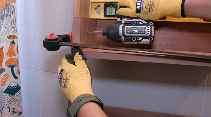 Una persona fija la segunda repisa del organizador para baño