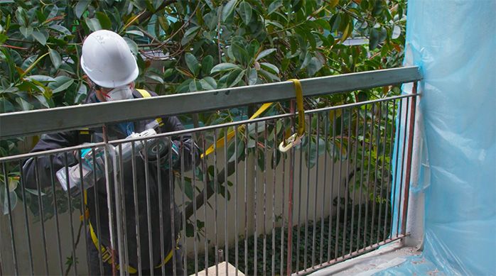 Una persona quita la pintura vieja de la baranda metálica por afuera de la terraza