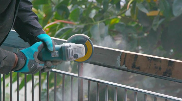 Una persona usa un esmeril angular con un disco flap para retirar la pintura vieja de la baranda de madera