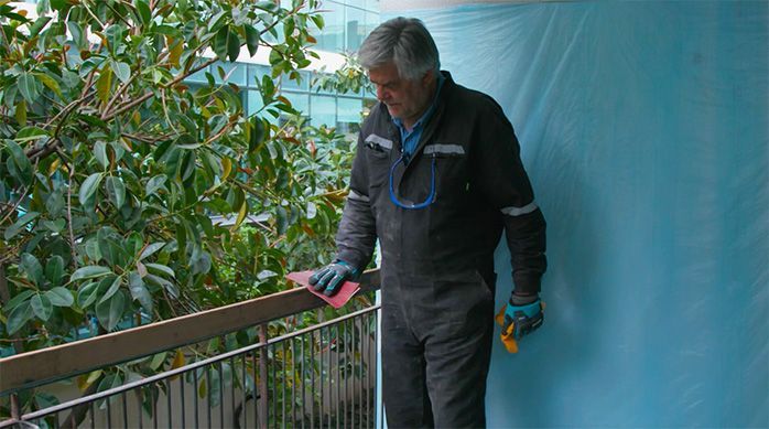 Una persona lija con una lija manual la baranda de madera