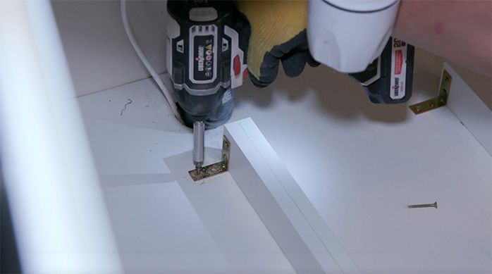 Una persona atornilla el vertical central en el mueble del lavaplatos