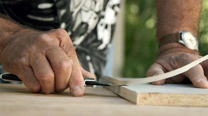 una persona corta el exceso de tapacanto con un cuchillo cartonero