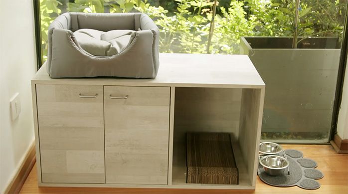 Mueble arenero para gatos terminado con una cama para gatos en la parte superior, un rascador para gatos en su interior y un tapete para mascotas con bebedero y comedero al lado