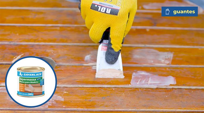 una persona con guantes aplica masilla de retape con una espátula en una mesa de madera