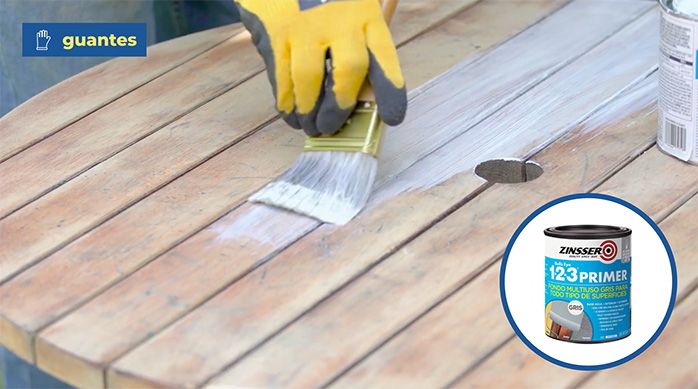 una persona con guantes aplica 1 2 3 primer con una brocha en la mesa de madera