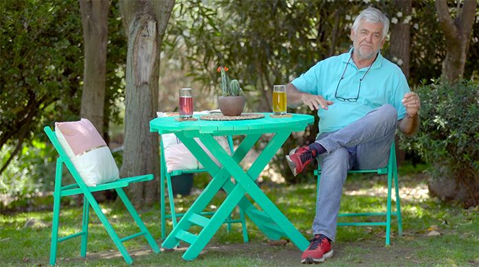 un hombre sentado en una silla para terraza turquesa junto a una mesa de madera restaurada de color turquesa