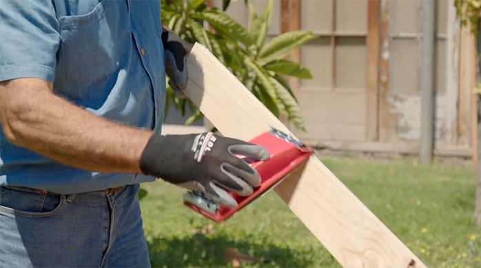 Una persona lija el pino seco cepillado con una lija y un soporte manual