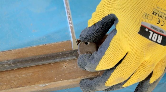 una persona con guantes usa un desatornillador manual para sacar la españoleta de una ventana de madera