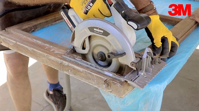 un hombre con guantes corta un marco de madera con una sierra circular