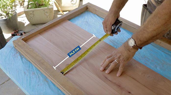 un hombre mide una tabla de madera en un marco de madera