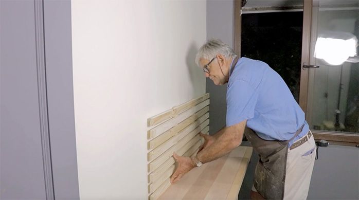 un hombre pega la rejilla decorativa del escritorio home office en el muro de la habitación