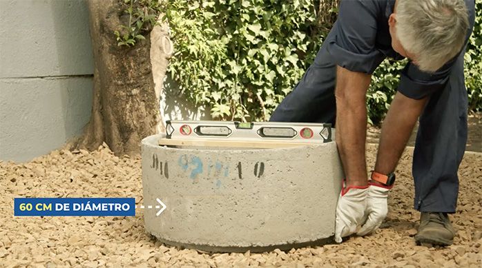 un hombre acomoda una cámara de alcantarillado de hormigón en el piso de un patio para armar un fogón de ladrillos.