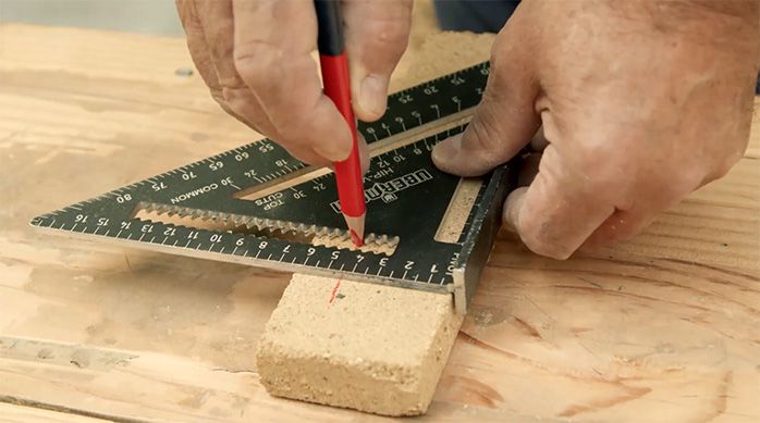un hombre marca un ladrillo refractario con un lápiz y una escuadra.