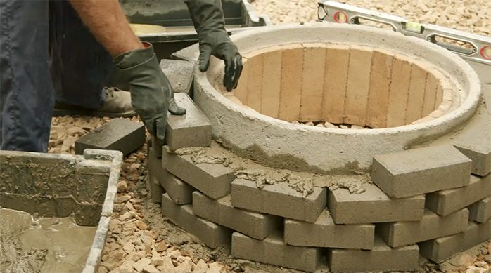una personas pega adocretos en la cara exterior de la cámara de alcantarillado para crear un fogón de ladrillos.