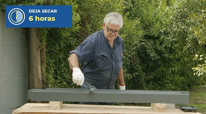 un hombre pinta tablas de pino seco cepillado con esmalte y un rodillo esponja.
