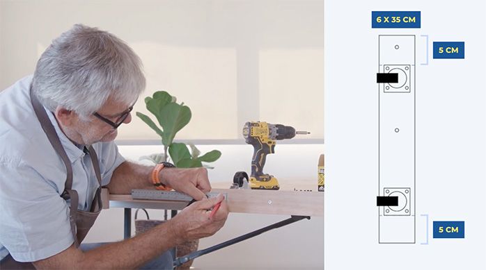 un hombre marca el lugar de las fijaciones para instalar ruedas en el separador de ambientes de madera